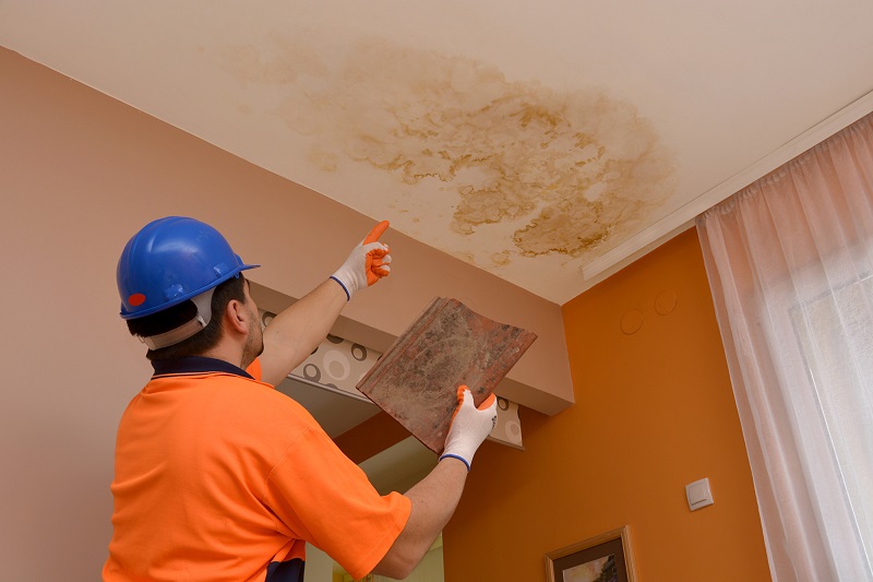 construction worker points to the place where the leaked water, holding the broken roof tile